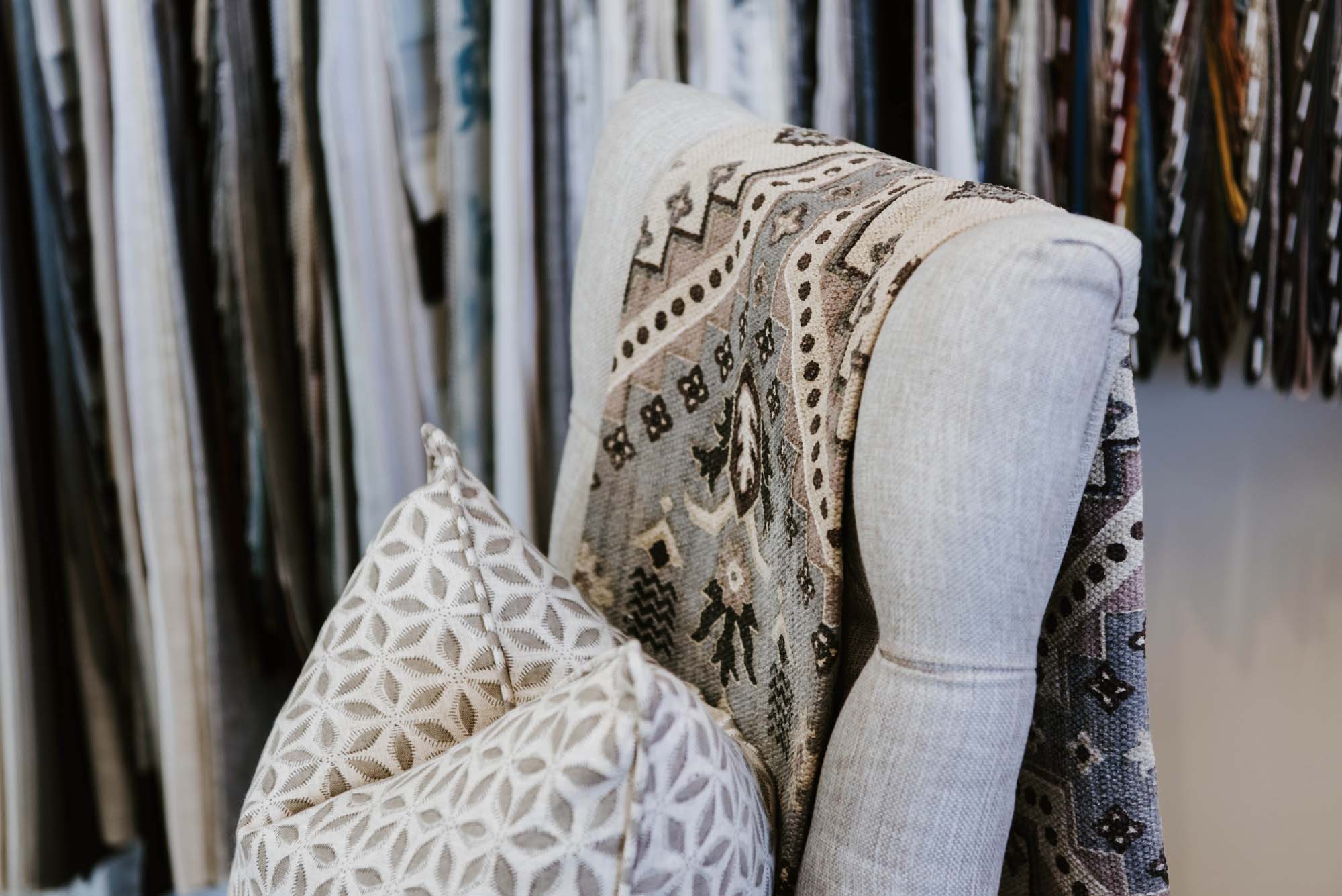 A chair with pillows in front of a rack of fabric.