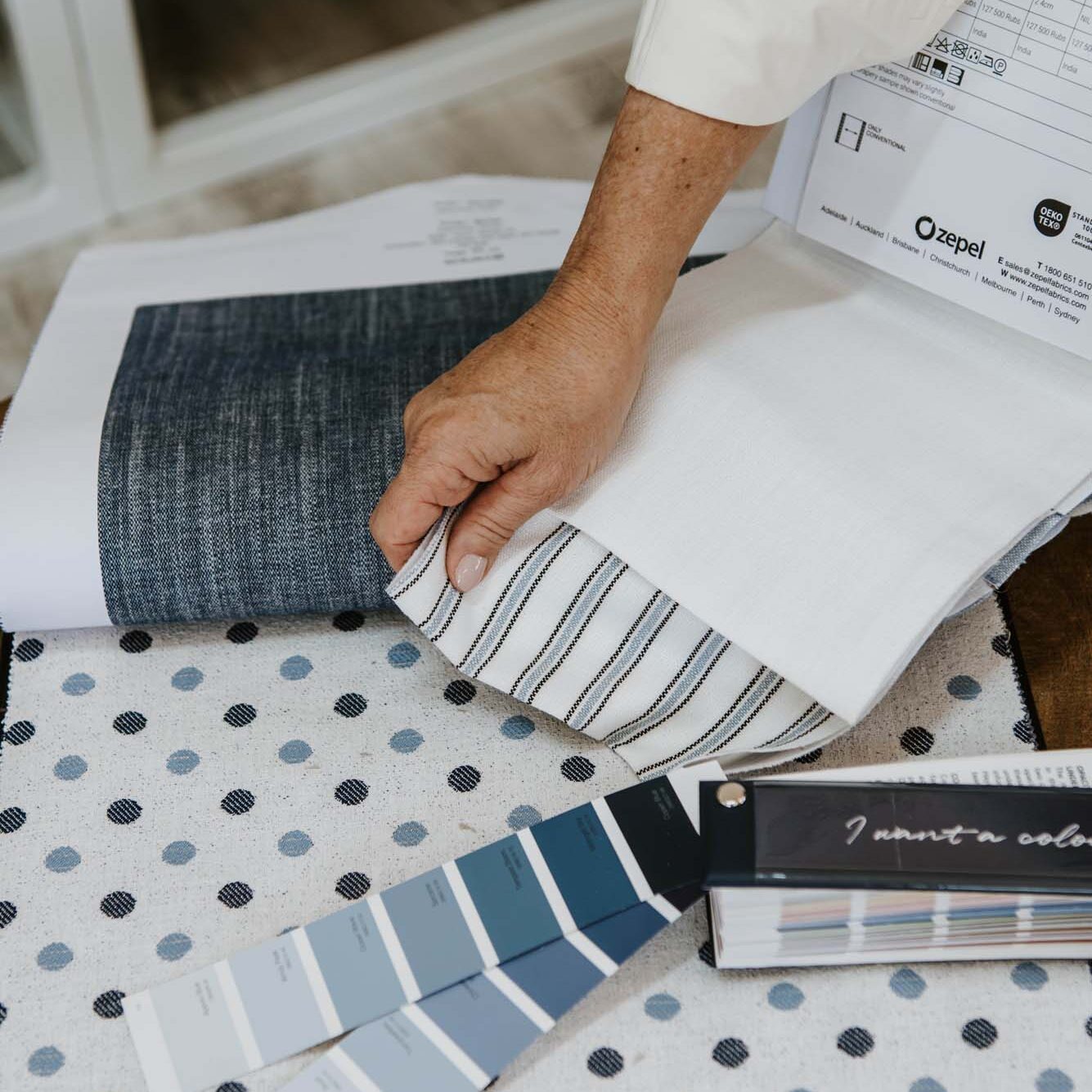 A hand laying out a fabric sample on a table.